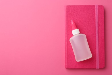 Glue and notebook on pink background, top view. Space for text