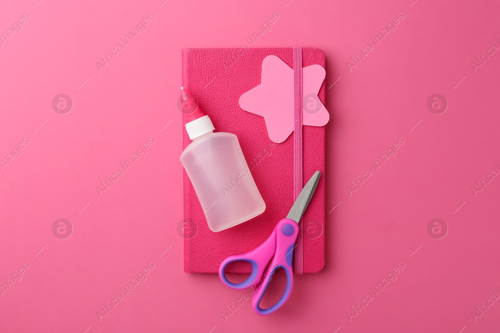 Photo of Glue, notebook and scissors on pink background, top view