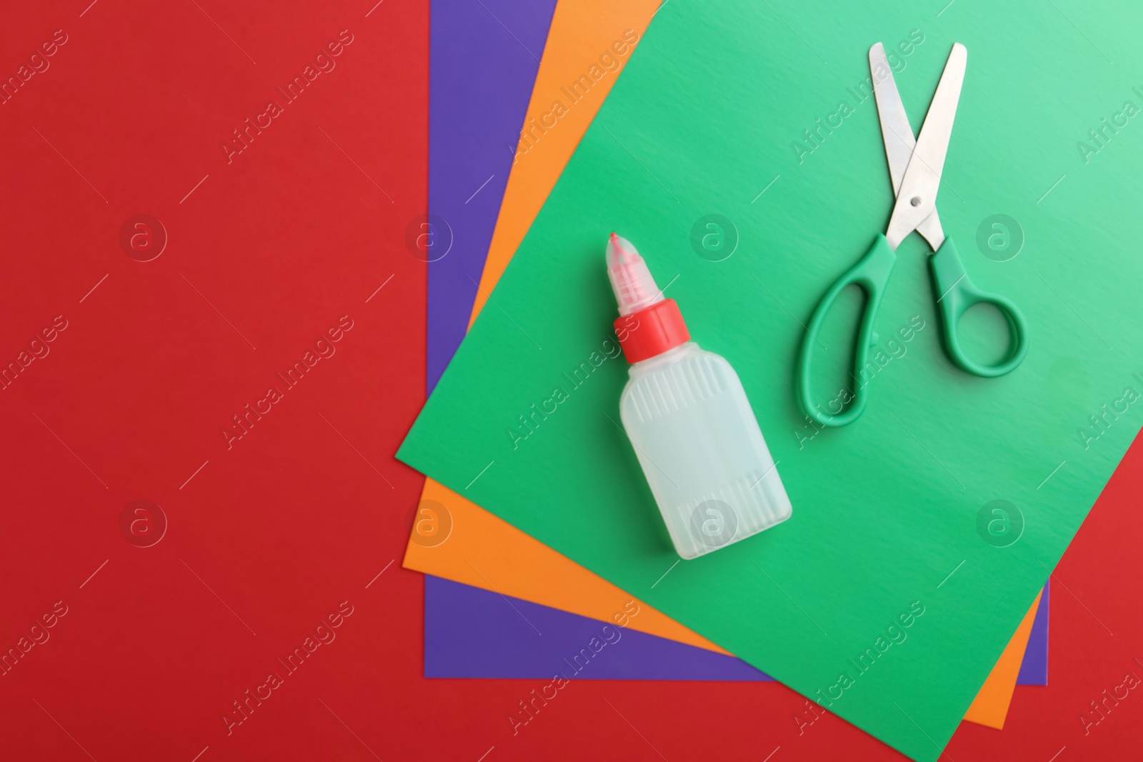 Photo of Bottle of glue, scissors and colorful paper on red background, flat lay. Space for text