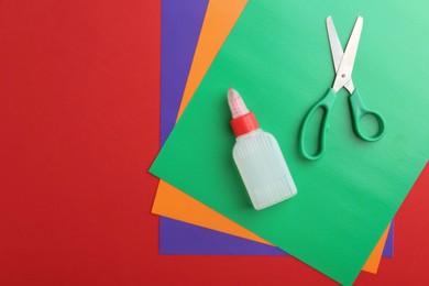 Bottle of glue, scissors and colorful paper on red background, flat lay. Space for text