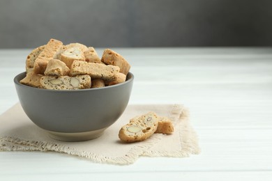 Photo of Traditional Italian almond biscuits (Cantucci) in bowl on white wooden table. Space for text