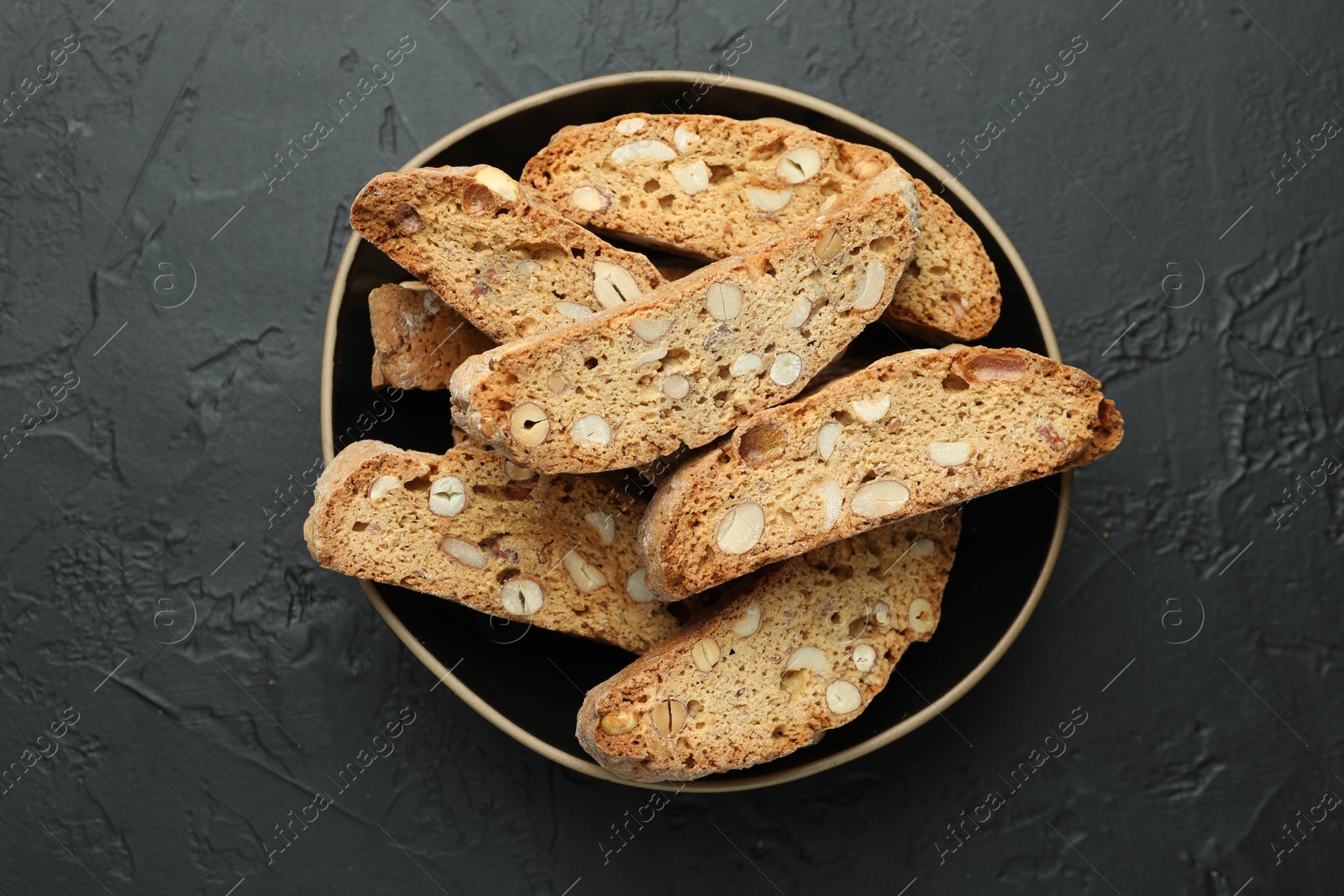 Photo of Traditional Italian almond biscuits (Cantucci) in bowl on black table, top view