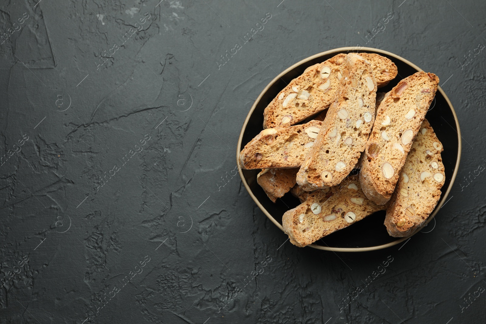 Photo of Traditional Italian almond biscuits (Cantucci) in bowl on black table, top view. Space for text