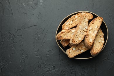 Traditional Italian almond biscuits (Cantucci) in bowl on black table, top view. Space for text