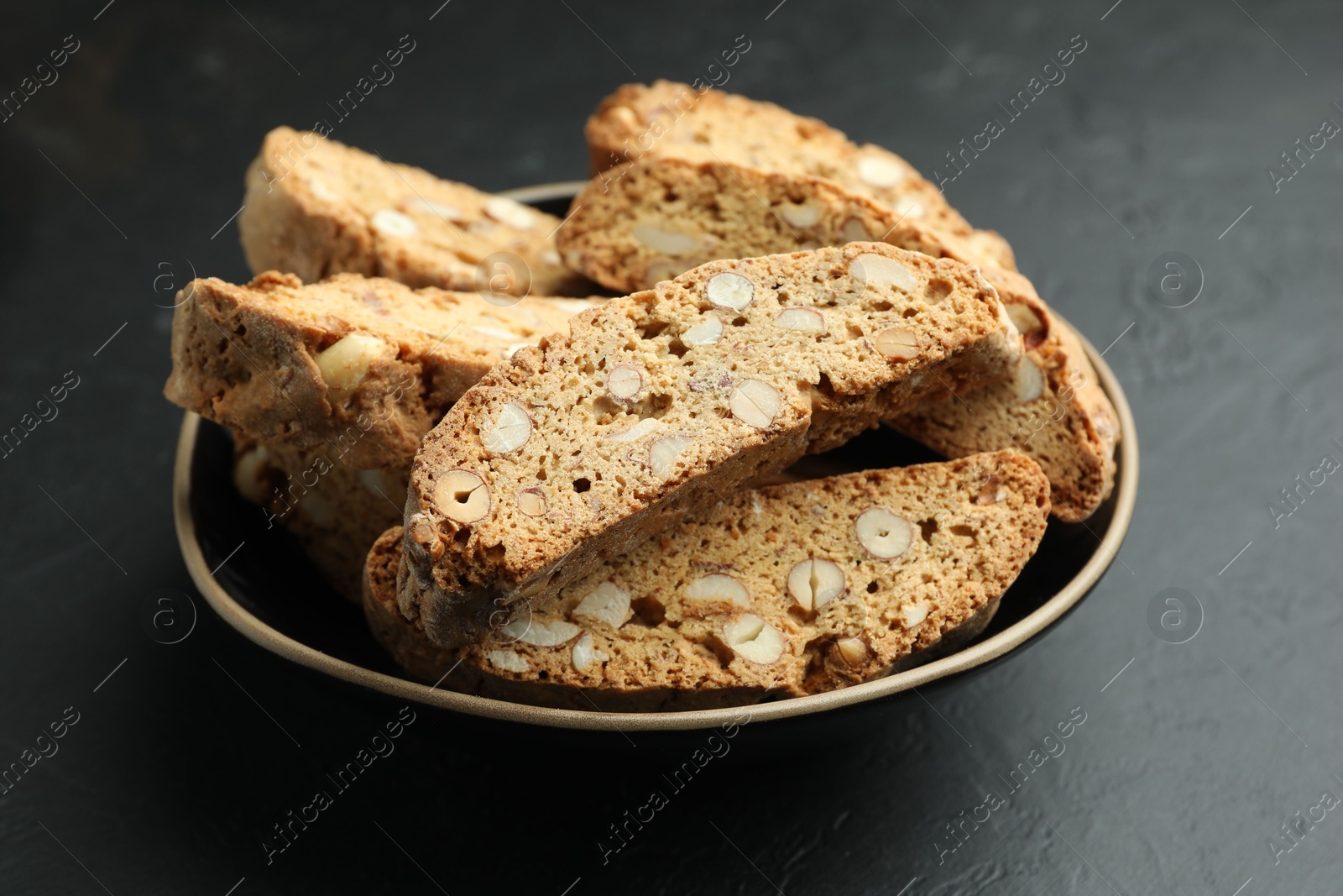 Photo of Traditional Italian almond biscuits (Cantucci) in bowl on black table, closeup