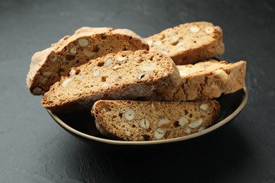 Photo of Traditional Italian almond biscuits (Cantucci) in bowl on black table, closeup