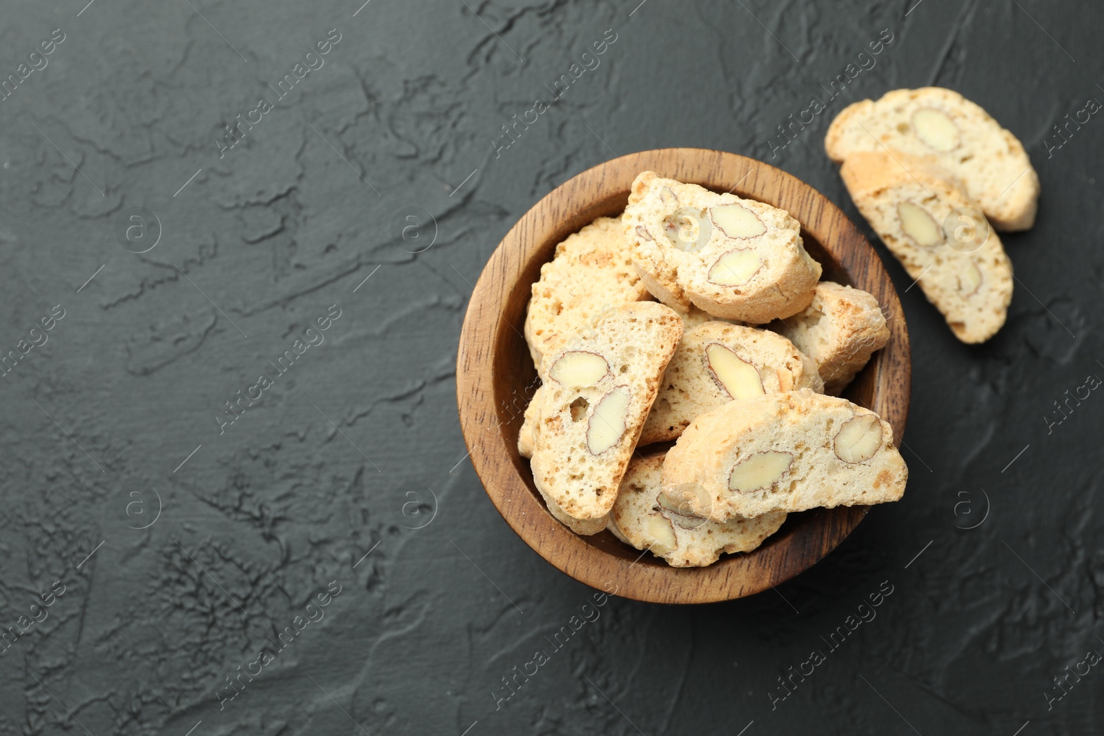 Photo of Traditional Italian almond biscuits (Cantucci) in bowl on black table, top view. Space for text