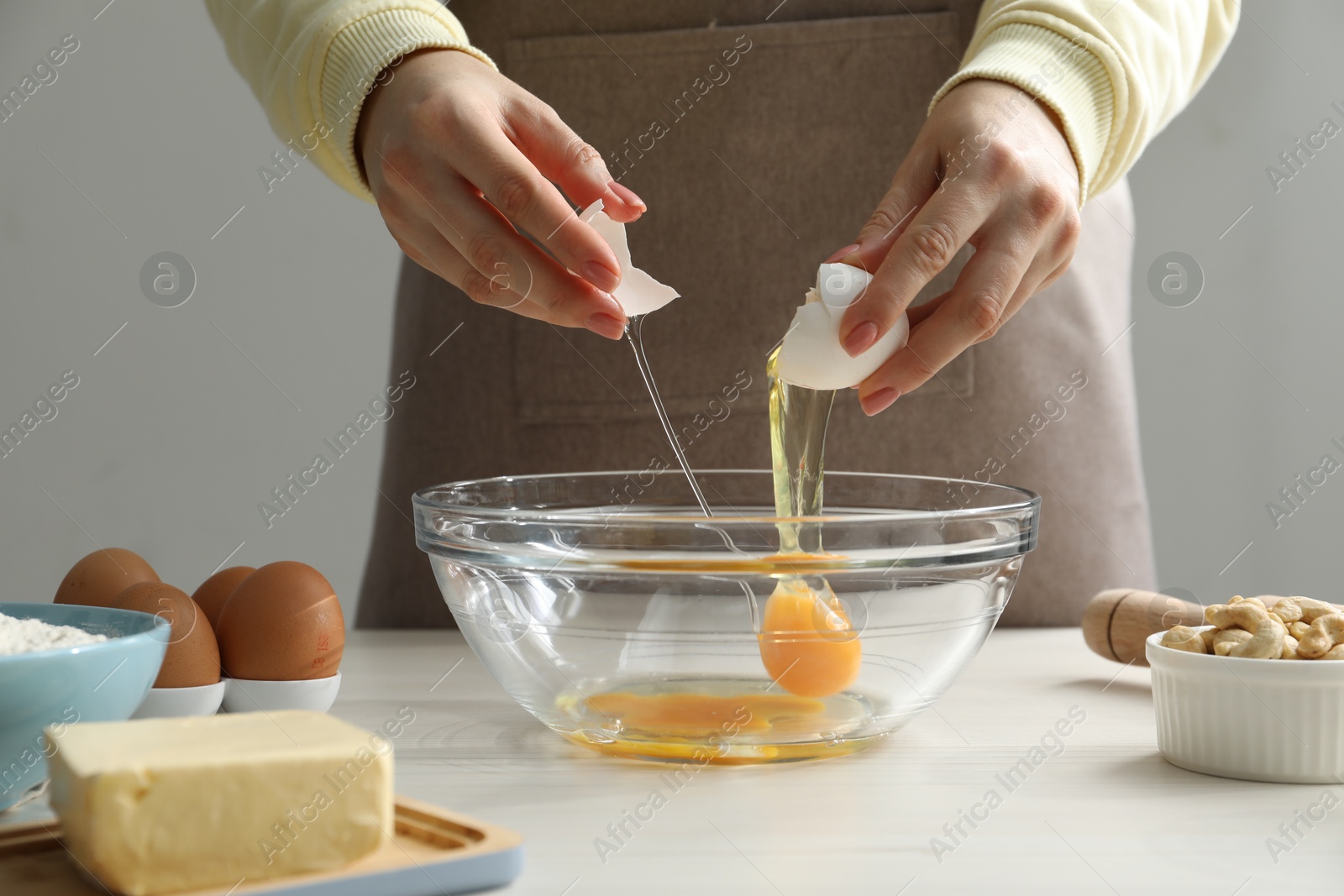 Photo of Making cashew cookies. Woman adding egg into bowl at white wooden table, closeup