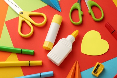 Glue, scissors and other stationery on color background, above view