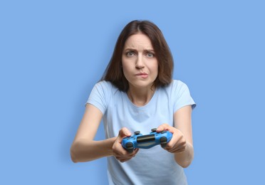 Emotional woman playing video game with controller on light blue background