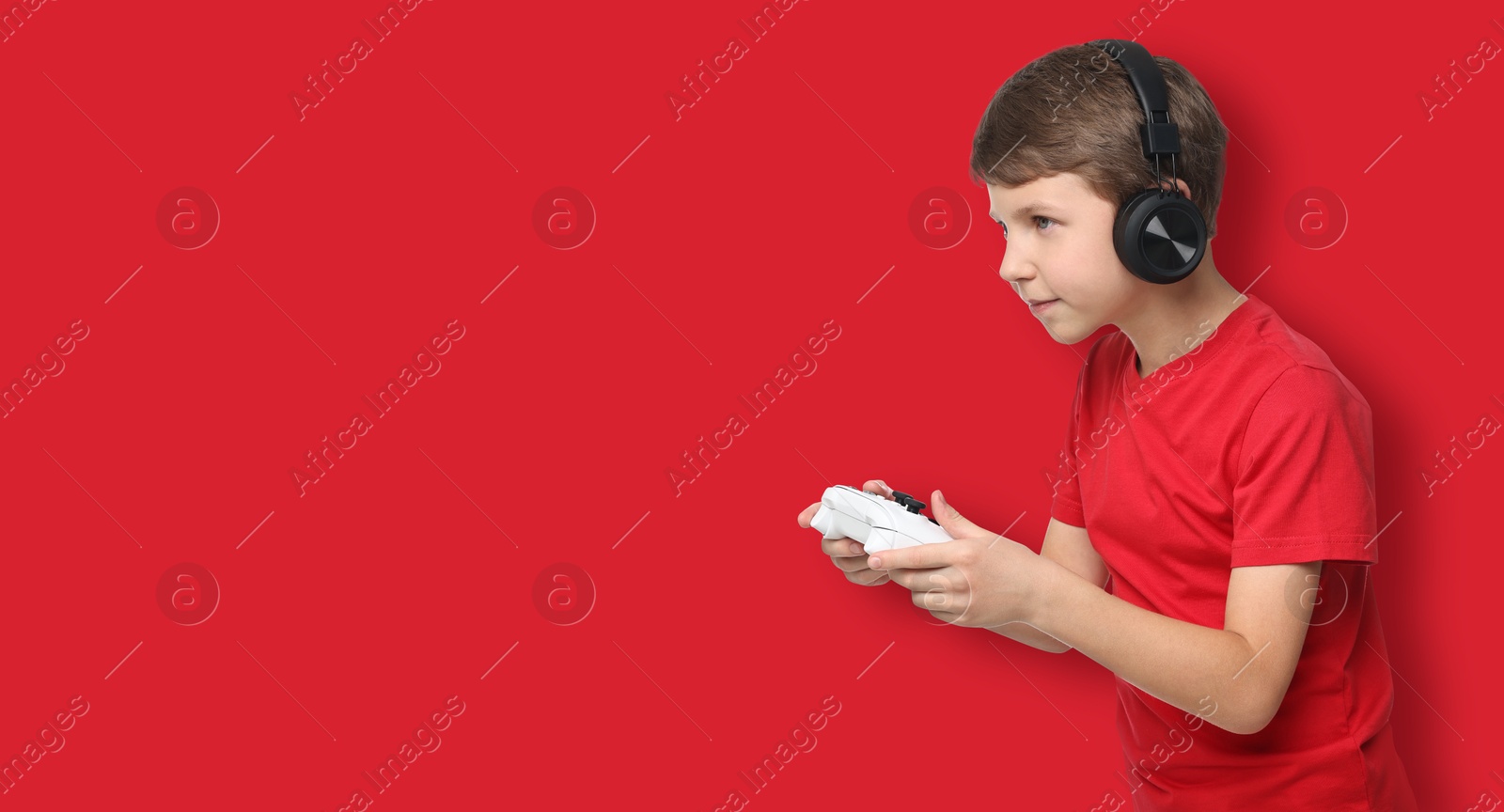 Image of Cute little boy in headphones playing video game with controller on red background. Banner design with space for text