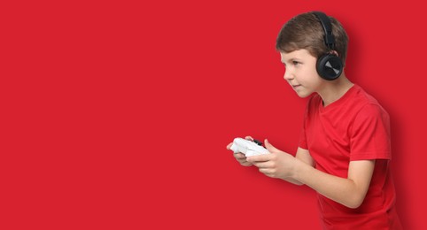 Cute little boy in headphones playing video game with controller on red background. Banner design with space for text