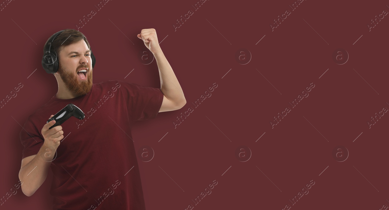 Image of Emotional man in headphones with game controller on brown background. Banner design with space for text