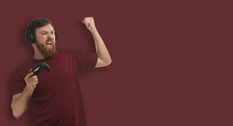 Emotional man in headphones with game controller on brown background. Banner design with space for text