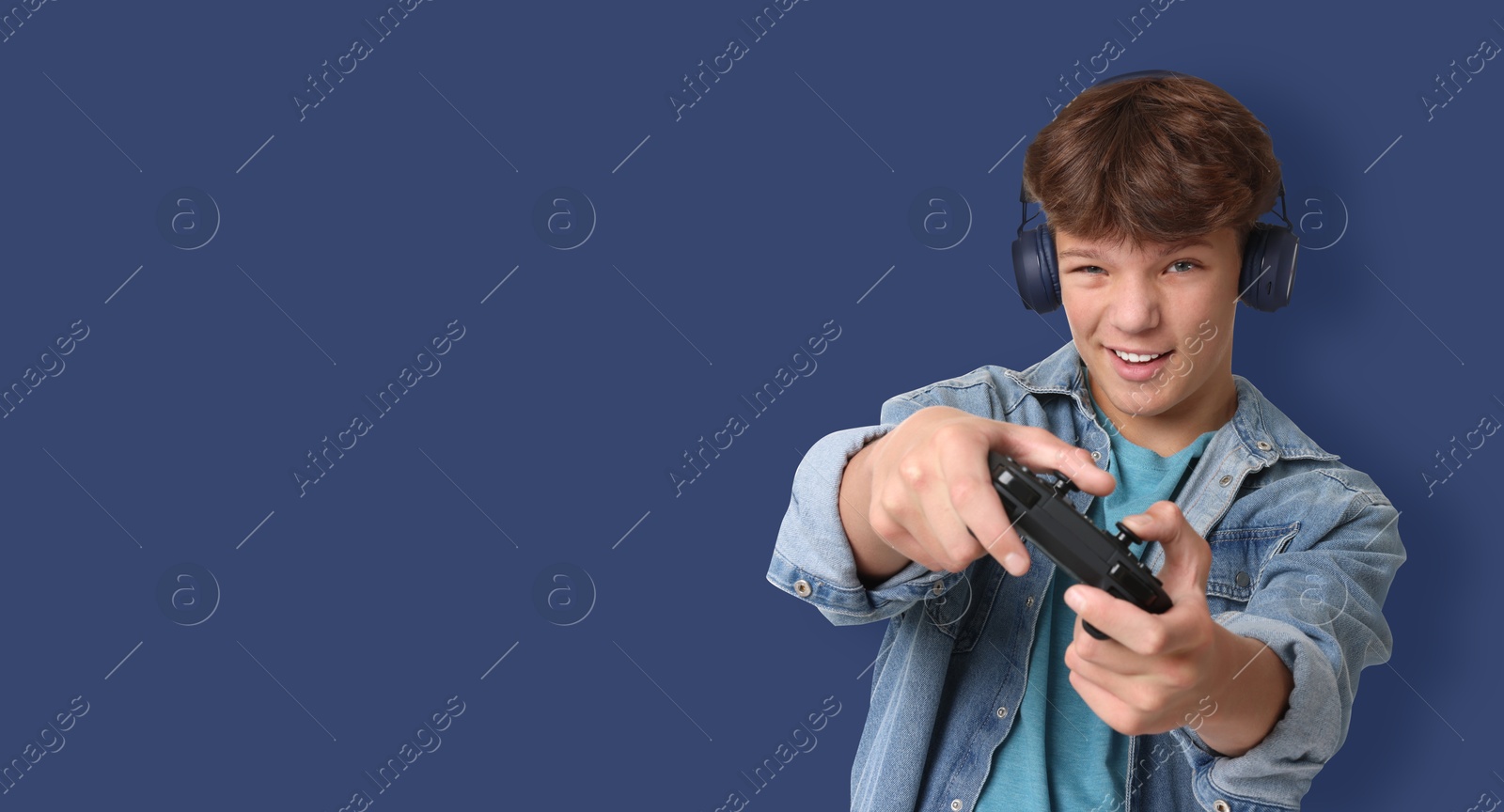 Image of Teenage boy in headphones playing video game with controller on blue background. Banner design with space for text