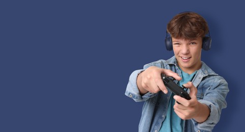 Teenage boy in headphones playing video game with controller on blue background. Banner design with space for text