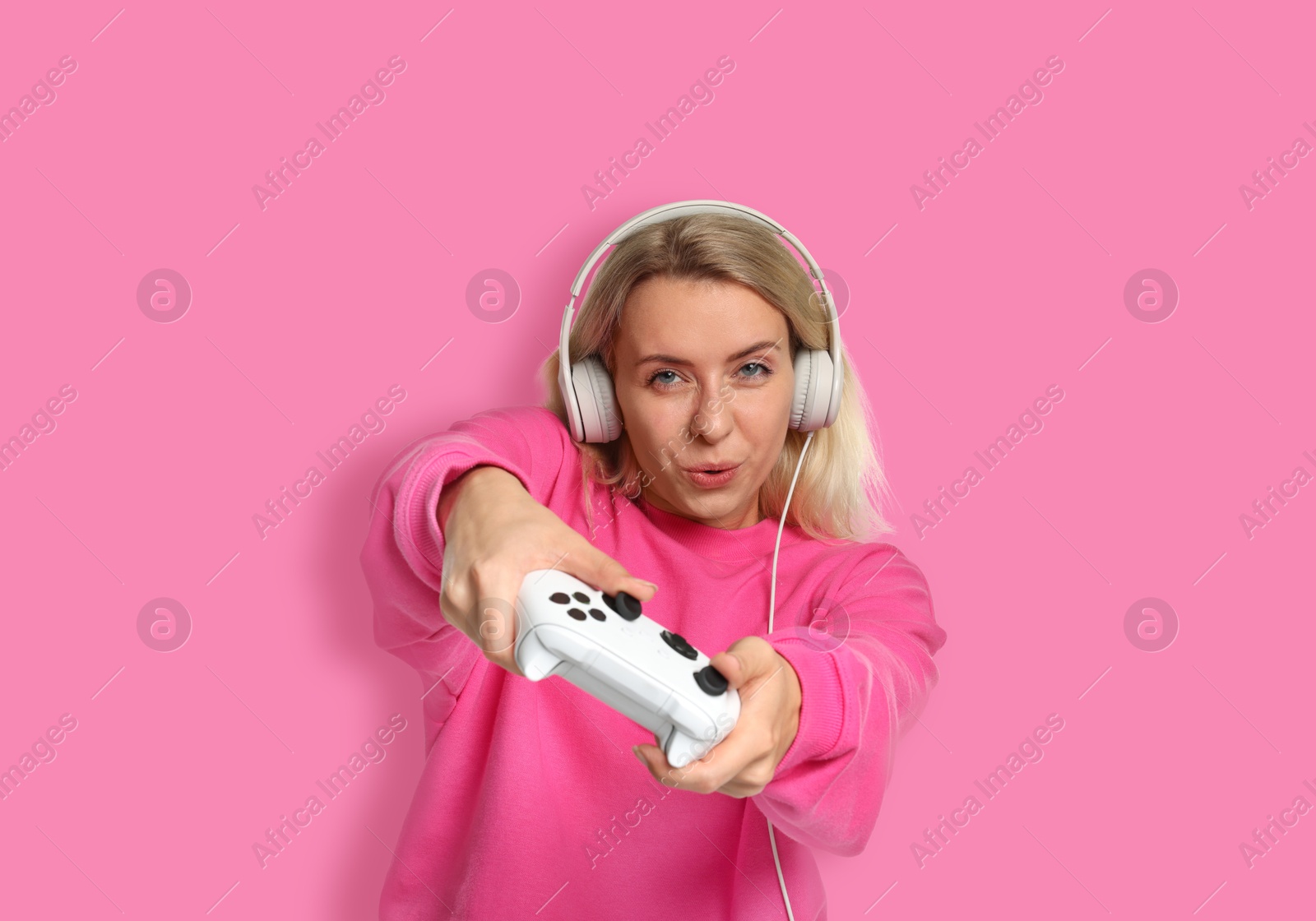 Image of Woman playing video games with controller on pink background