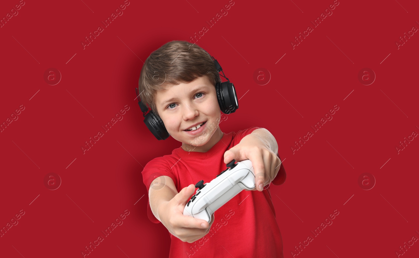 Image of Happy little boy in headphones playing video game with controller on red background