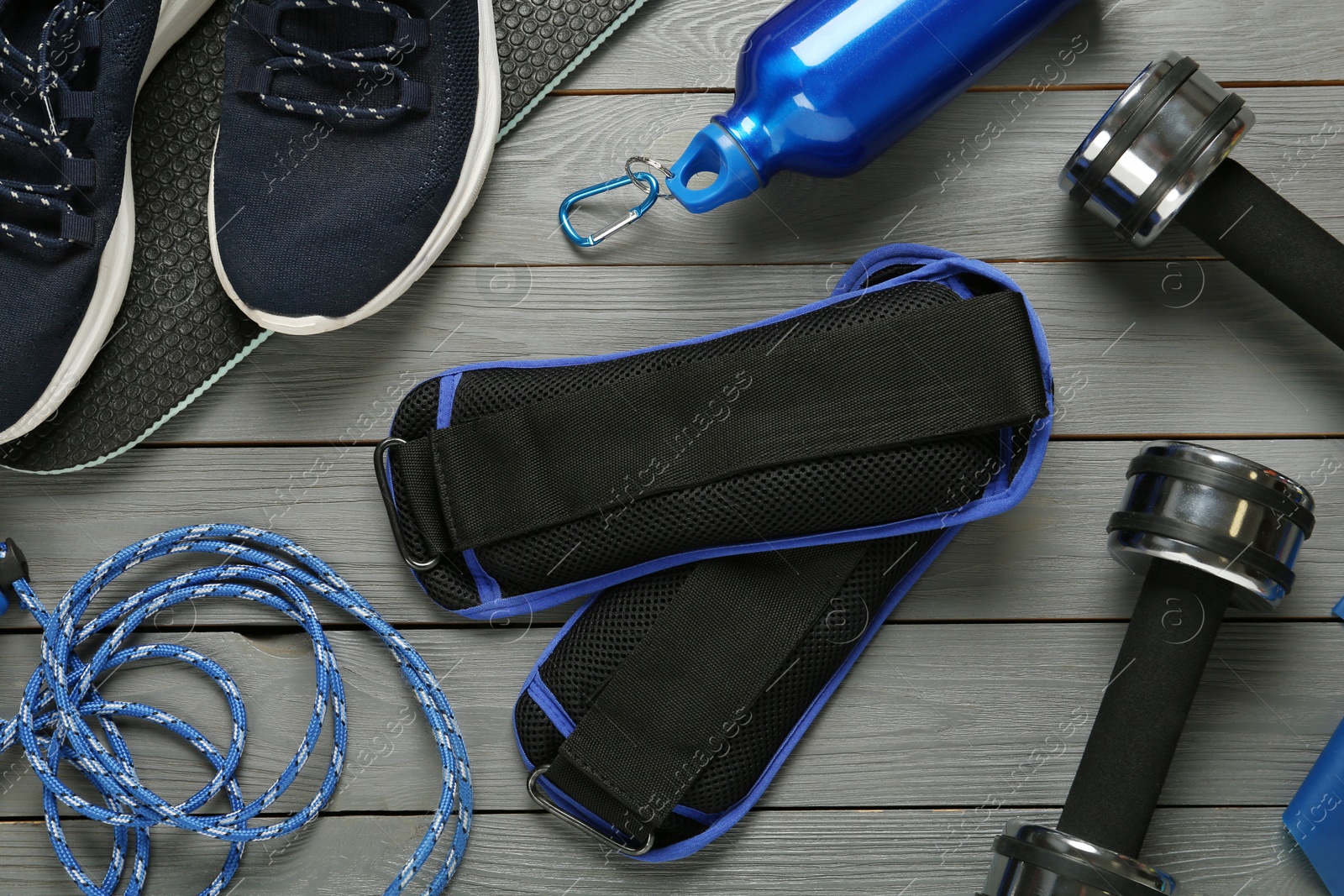 Photo of Blue ankle weights and sport equipment on grey wooden table, flat lay