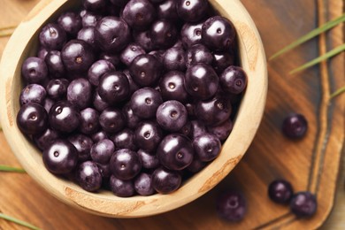 Photo of Ripe acai berries in bowl on wooden table, flat lay