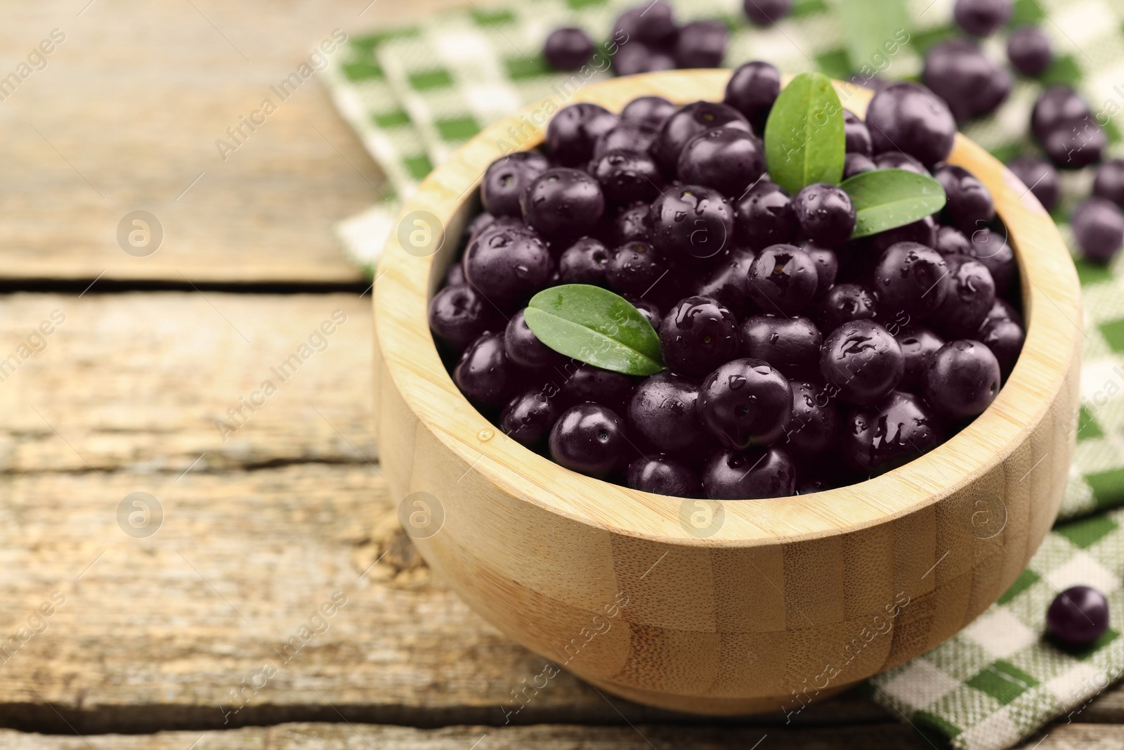 Photo of Ripe acai berries and leaves in bowl on wooden table, closeup. Space for text