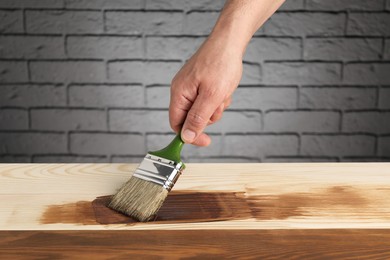 Photo of Man with brush applying walnut wood stain onto wooden surface, closeup