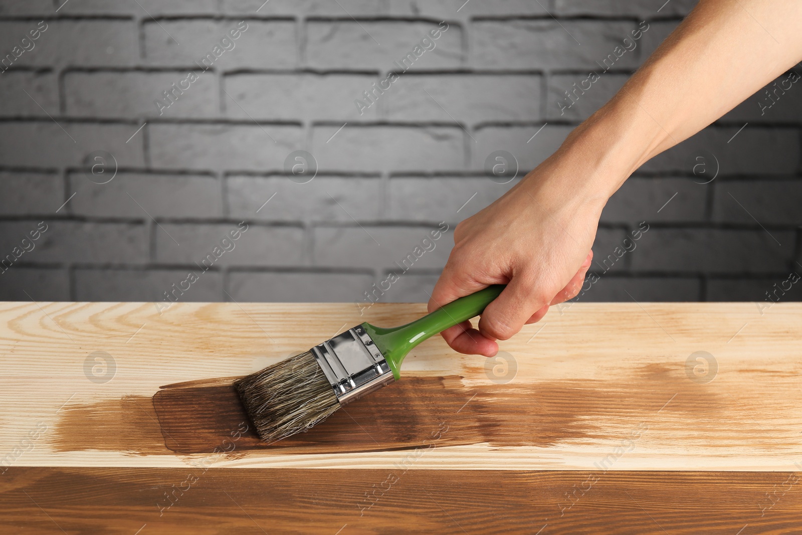 Photo of Man with brush applying walnut wood stain onto wooden surface, closeup