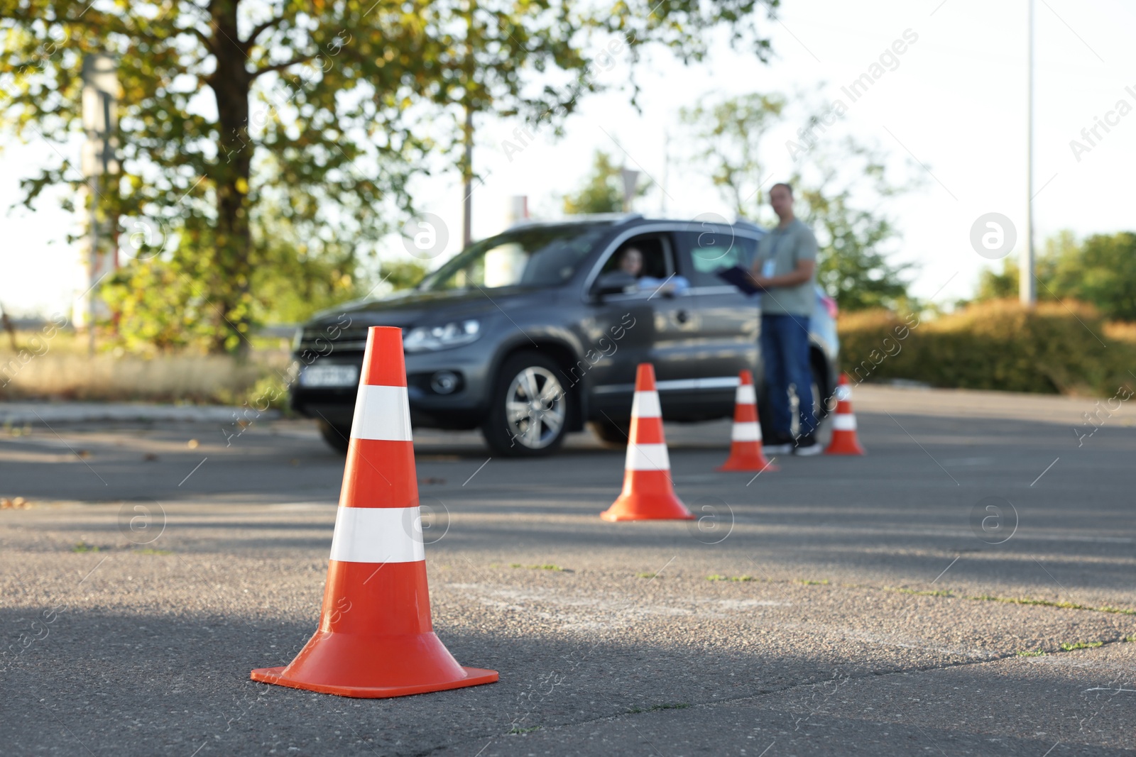 Photo of Examiner instructing student before exam at driving school test track, focus on traffic cone