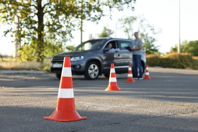 Examiner instructing student before exam at driving school test track, focus on traffic cone