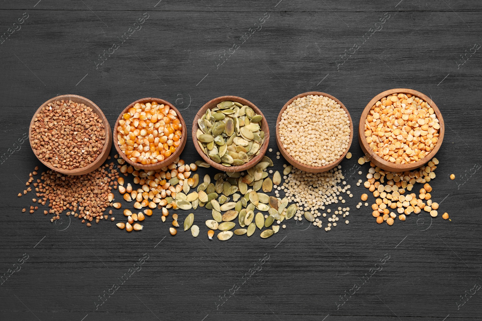 Photo of Different types of seeds and cereals in bowls on black wooden table, flat lay