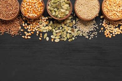 Different types of seeds and cereals in bowls on black wooden table, flat lay. Space for text