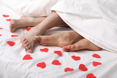 Couple lying in bed with red paper hearts, closeup