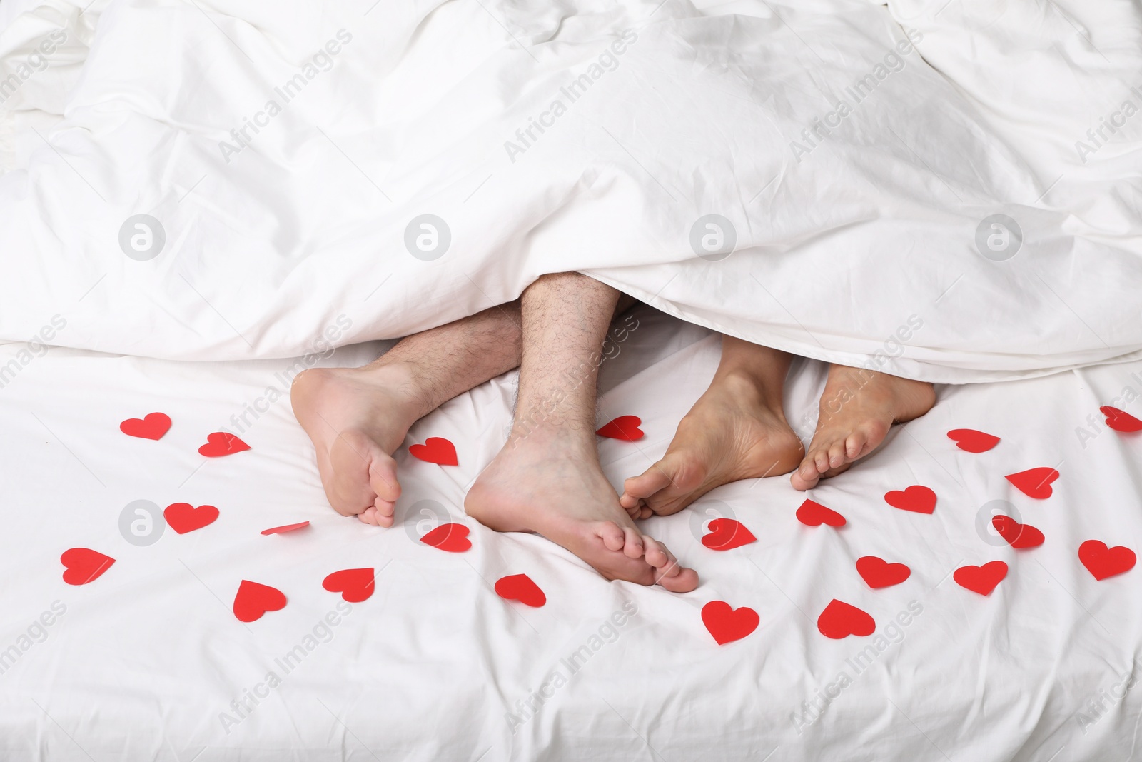 Photo of Couple lying in bed with red paper hearts, closeup