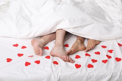 Couple lying in bed with red paper hearts, closeup