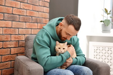 Man petting cute ginger cat on armchair at home