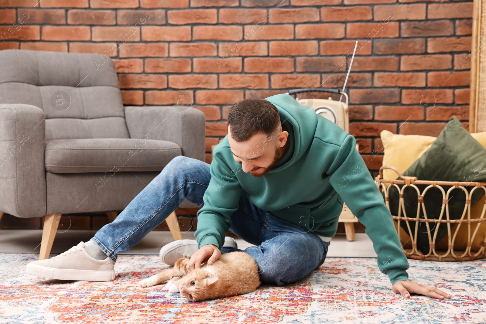 Photo of Man petting cute ginger cat on floor at home