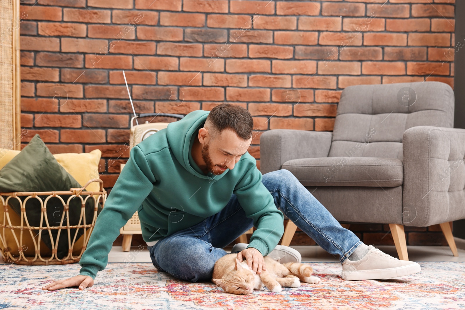 Photo of Man petting cute ginger cat on floor at home