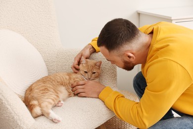 Man petting cute ginger cat on armchair at home