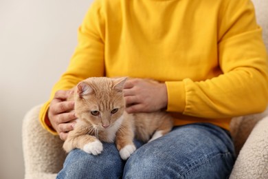 Photo of Man petting cute ginger cat on armchair at home, closeup