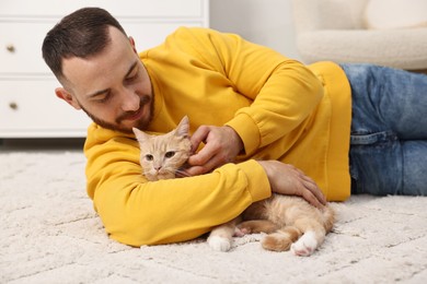 Man petting cute ginger cat on floor at home