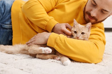 Man petting cute ginger cat on floor at home