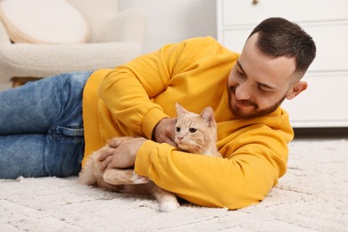 Man petting cute ginger cat on floor at home