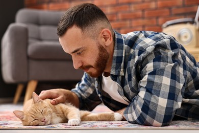 Photo of Man petting cute ginger cat on floor at home