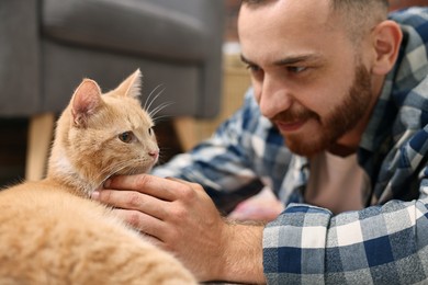 Photo of Man petting cute ginger cat on floor at home