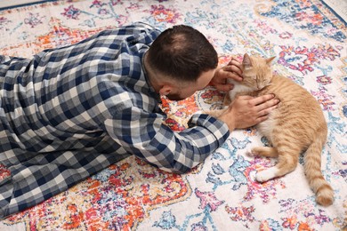 Photo of Man petting cute ginger cat on floor at home