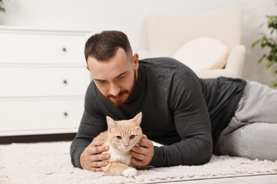 Man petting cute ginger cat on floor at home