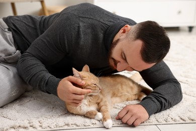 Photo of Man petting cute ginger cat on floor at home