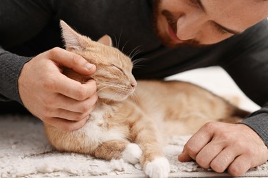 Photo of Man petting cute ginger cat on floor at home, closeup