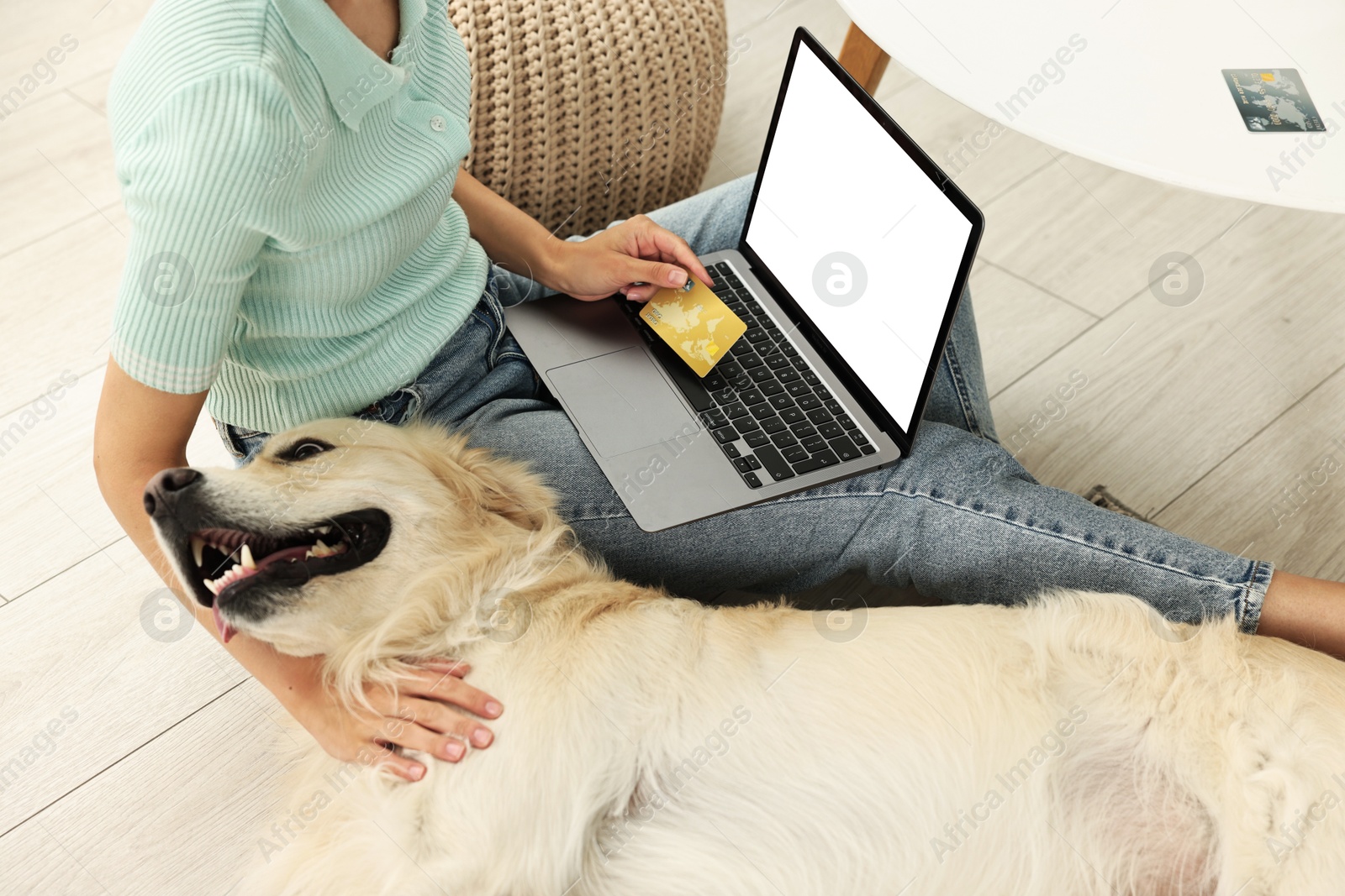 Photo of Online pet shop. Woman with laptop, credit card and cute Golden Retriever dog making order at home, closeup