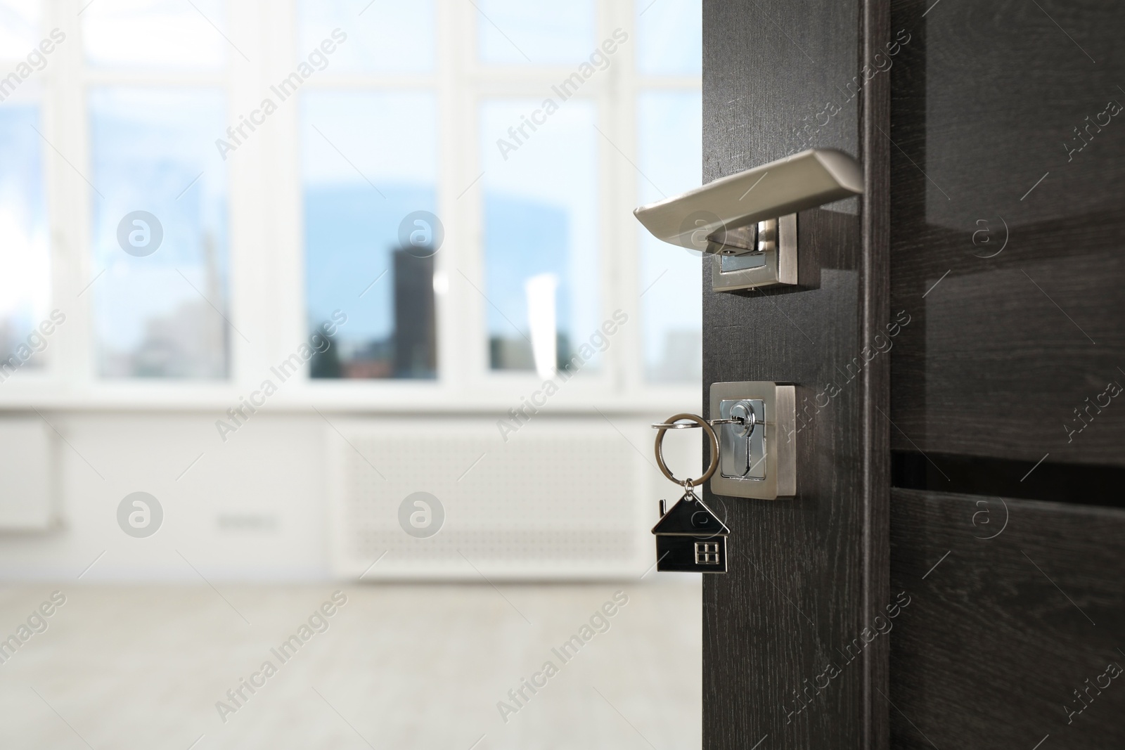 Photo of Open door with key and house shaped keychain, closeup. Space for text